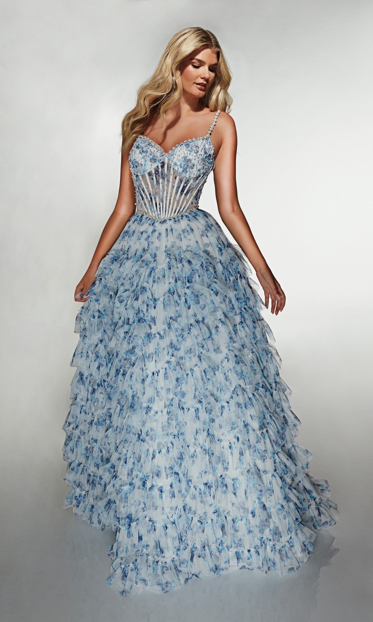 Woman wearing the Alyce 62182 long prom dress—featuring a blue and white floral print, fitted sheer corset bodice, and layered ruffled skirt—stands against a plain background, showcasing an elegant modern prom look.